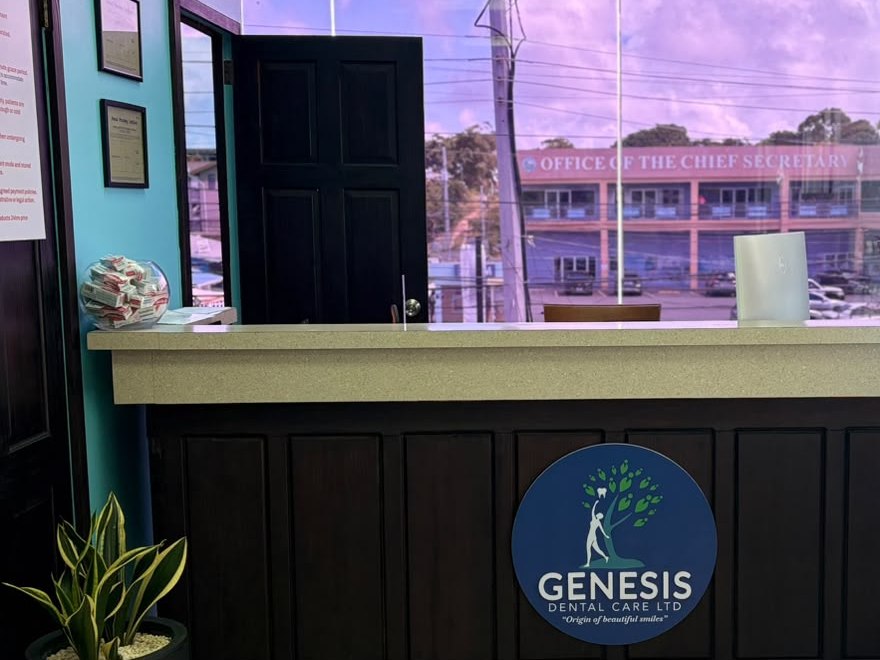 The reception desk at Genesis Dental Care in Crown Point, Tobago, with the clinic logo on the front and a view over Crown Point through the window.